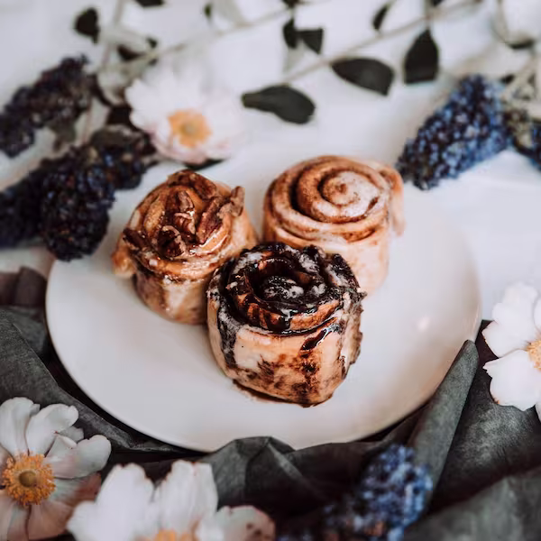 Cinnamon rolled topped with icing served on a plate, with white flowers in the foreground and background