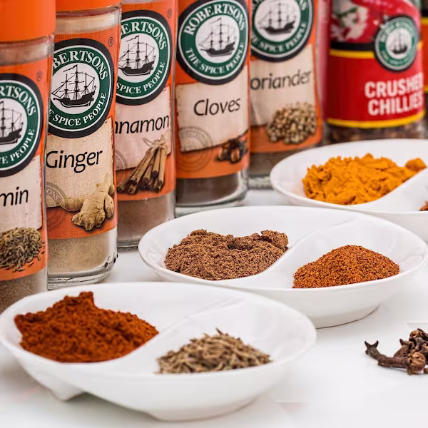 Sealed glass jars of various spices with some of their contents placed in small ceramic plates in front of them