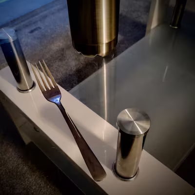 A stainless steel four-tooth fork on a reflective table top made of transparent glass